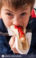 an-eleven-year-old-boy-eating-a-hot-dog-with-tomato-ketchup-sauce-C36H0J.jpg